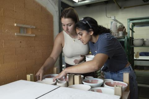 Two students placing ceramic pieces into a kiln in the AUArts ceramics studio.