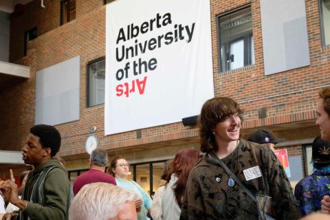 Why choose AUArts? Students gather in AUArts’ main hall during orientation, chatting under a large Alberta University of the Arts banner.