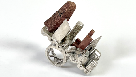 Sculptural silver ring with miniature architectural forms, including red and metallic building-like structures.