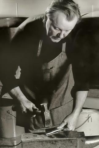Orland Larson hammering metal at the bench. 