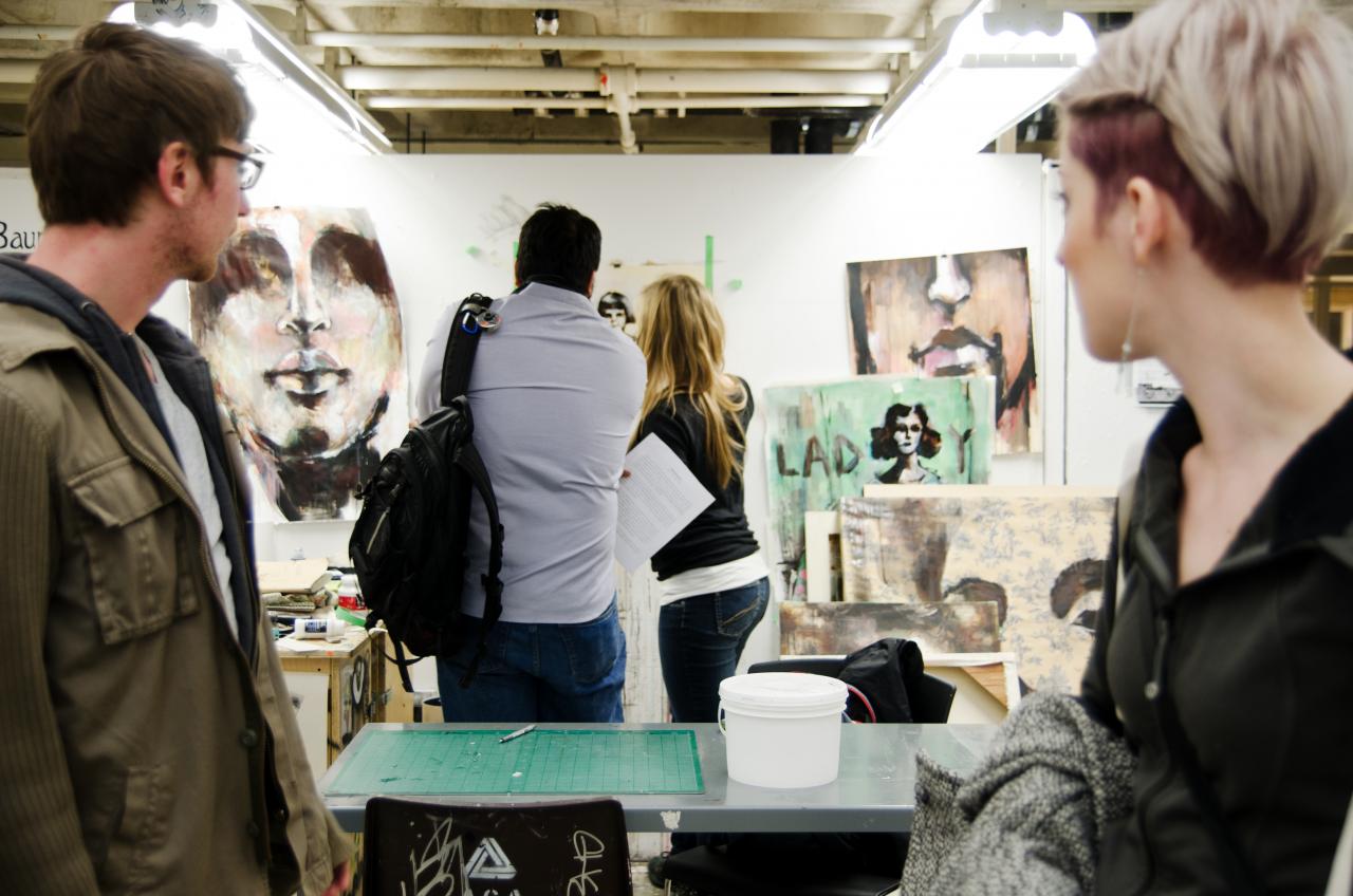 a group of students views paintings of faces in an art studio