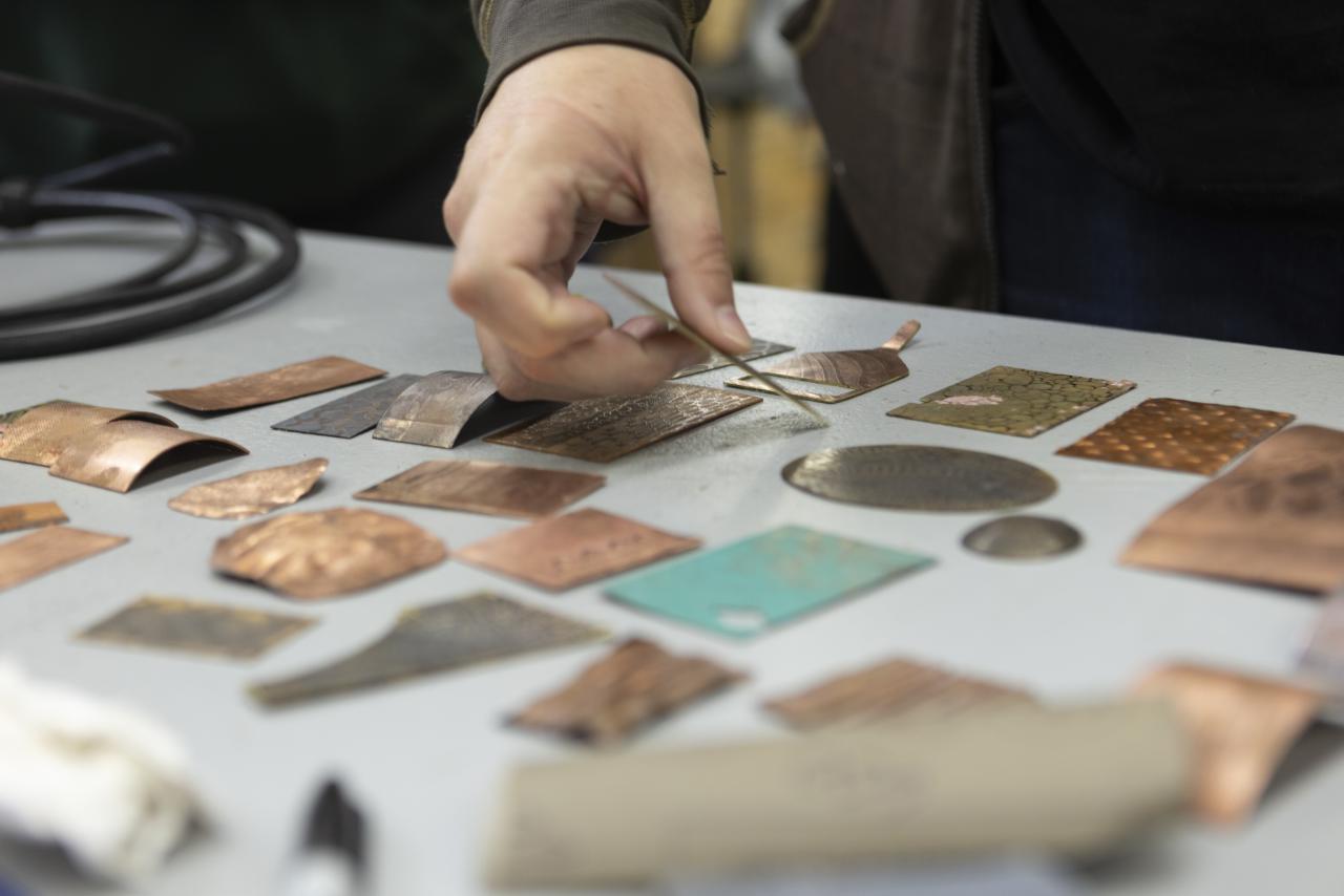 Close-up of a student arranging textured and etched metal pieces on a table in the AUArts jewelry and metals studio.