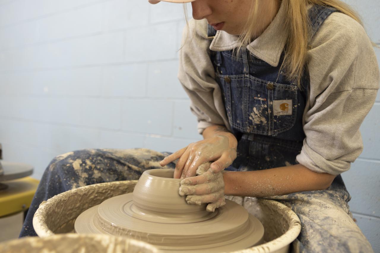 Student shaping clay on a pottery wheel in the AUArts ceramics studio.
