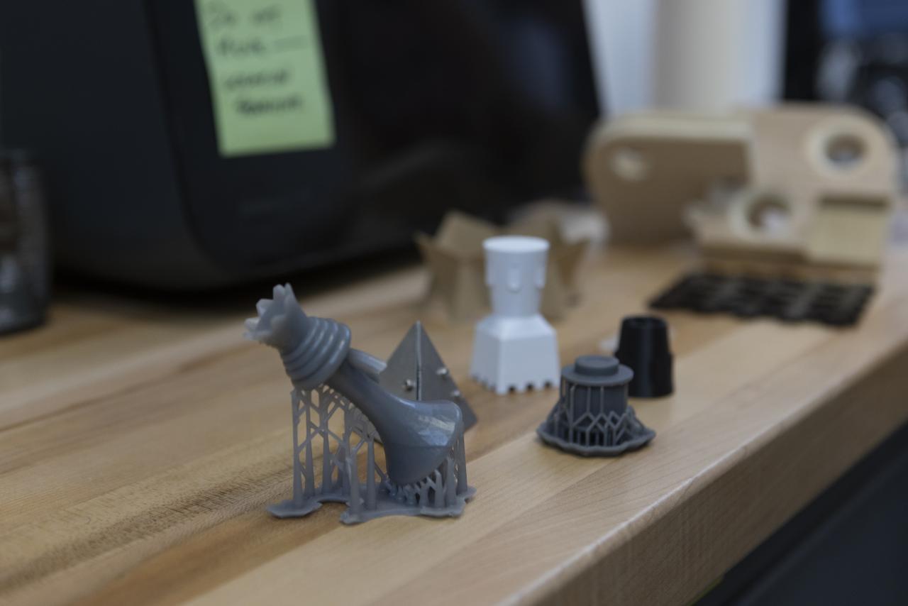 Close-up of small 3D-printed objects in various shapes and colors displayed on a wooden workbench.