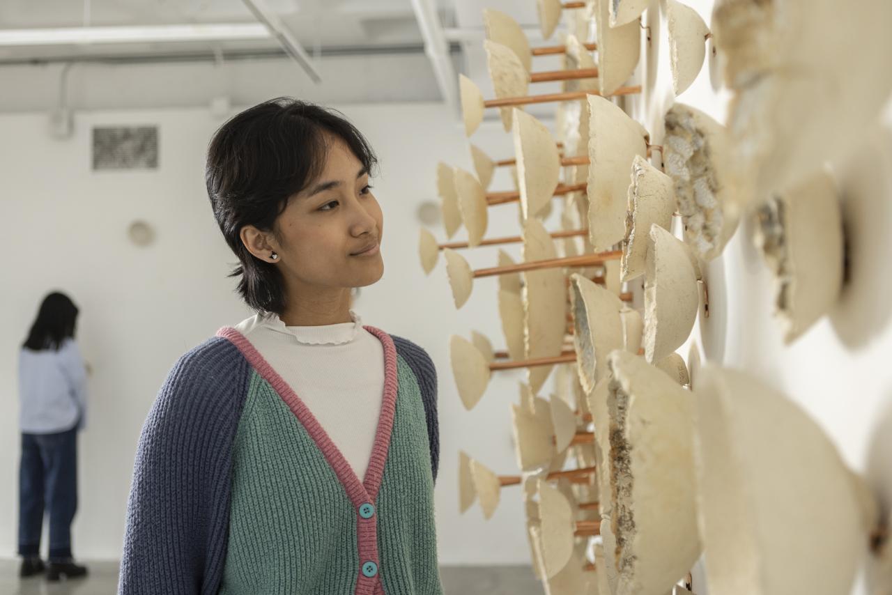 Student observing a wall-mounted ceramic installation in an AUArts gallery space.