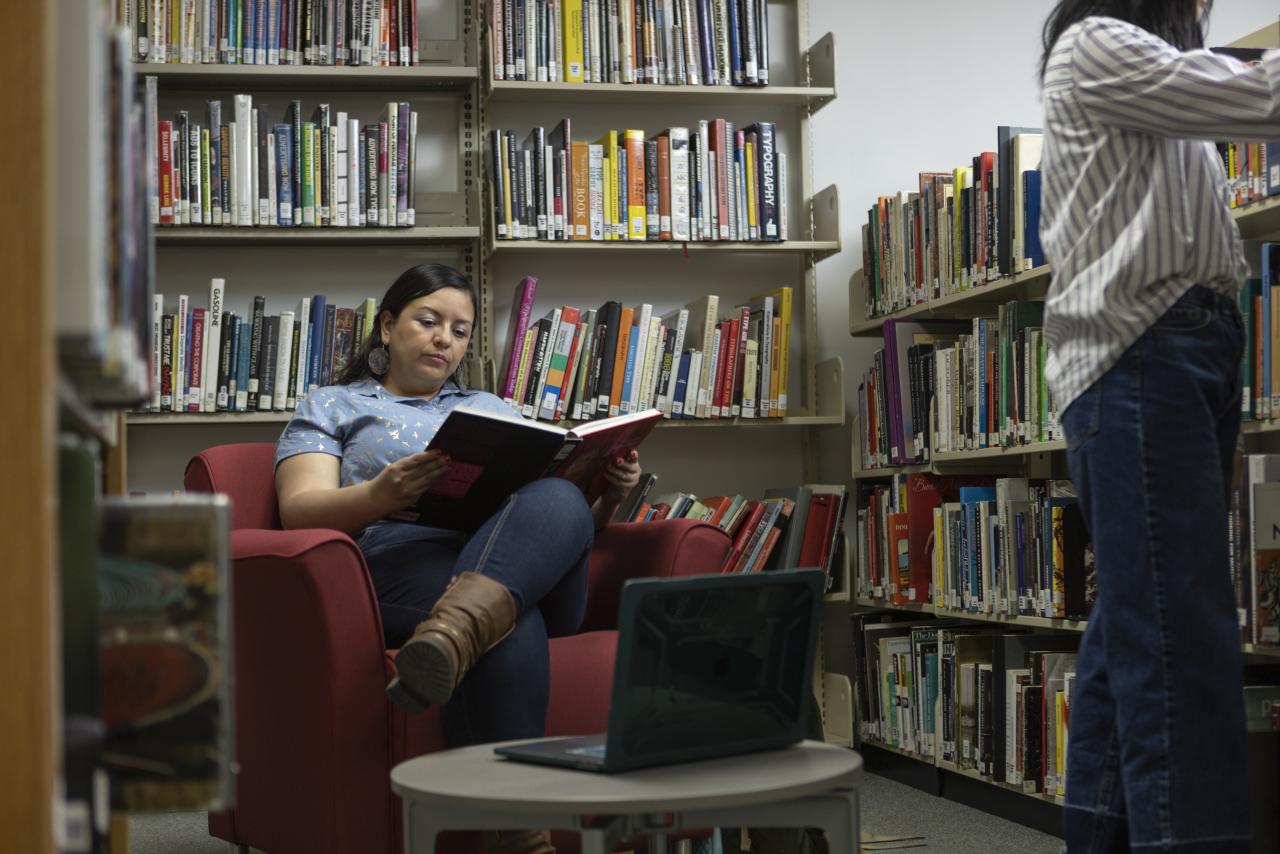 Student reading a book while seated in a red chair in the AUArts library.