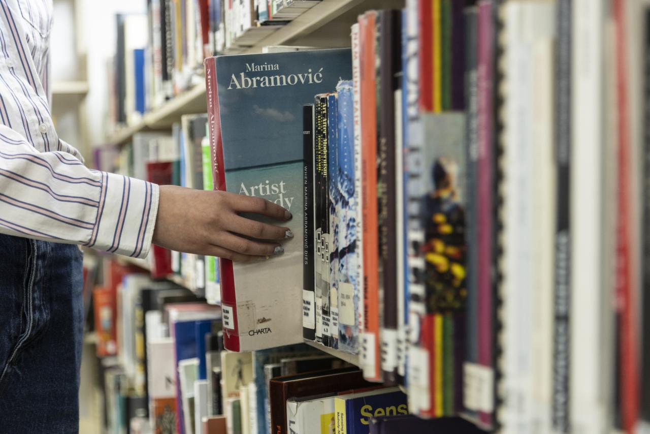 Student pulling a book titled Marina Abramović: Artist Body from a library shelf at AUArts.