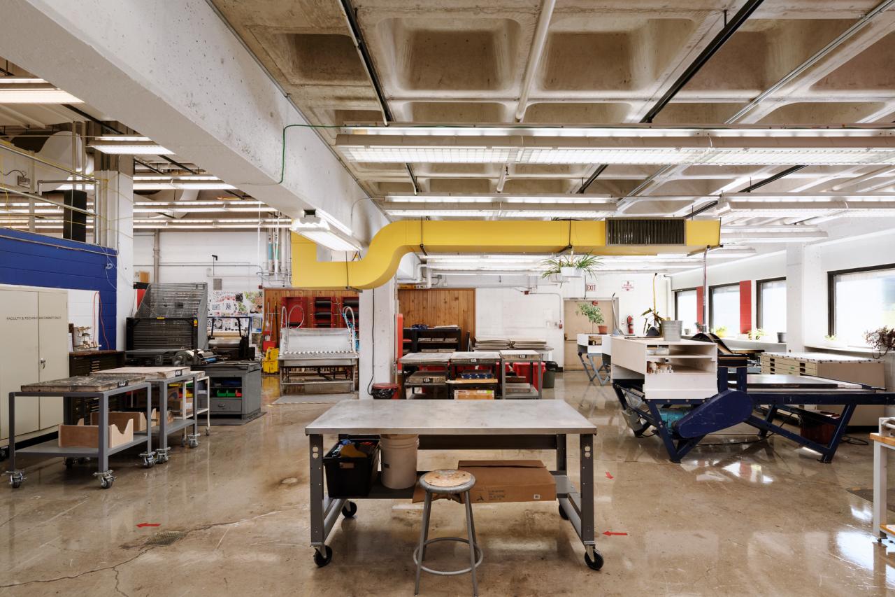 Printmaking workspace with long worktables, sinks, and printing equipment, set against colorful red, blue, and white walls.