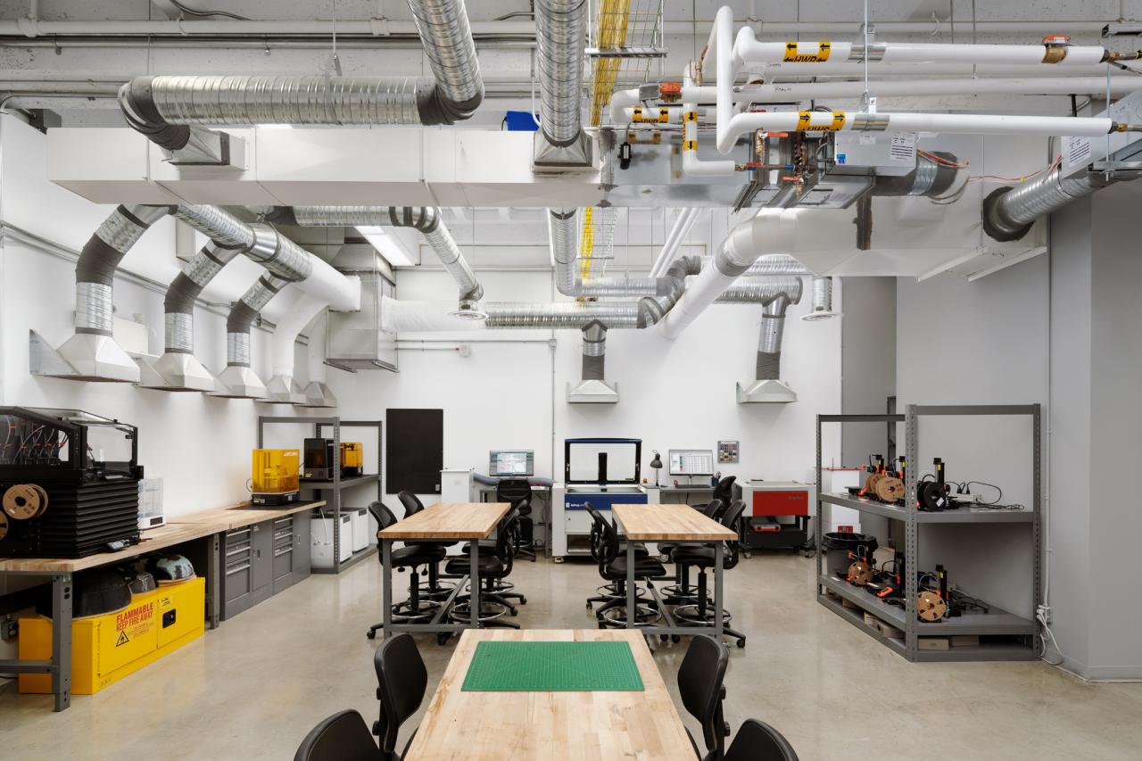 Object Design's Thing Tank Studio Bright workshop space with wooden tables, computers, and shelves of 3D printers and fabrication equipment, featuring exposed ducts and ventilation overhead.