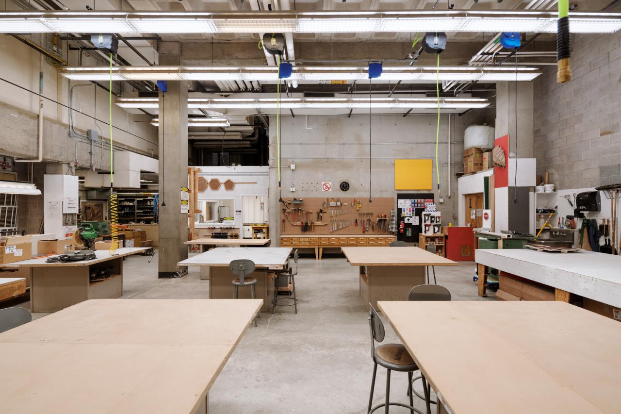 AUArts wood shop with large workbenches, hanging power cords, and tool stations organized along the back wall.