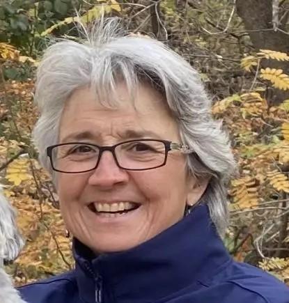 profile photo of educational technician, Lisa Cerny, wearing a blue jacket and black rectangular glasses, standing in nature.