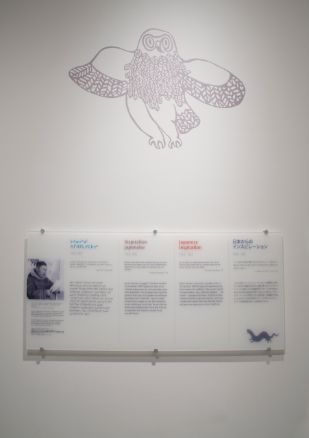 Informative text on plastic panels is hung on the wall. 1959-1963, "Japanese Inspiration". James Houston returns to Canada, his print shown at an exhibition inspired Inuit printmakers who adapted Japanese techniques into their work giving new expression to Inuit traditions.