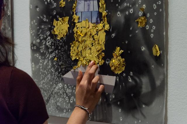 Detail of gallery attendee offering gold leaf to a water colour triptych . Heather Hart. New Numinous Negro: Mildred Lewis I,II,III. 2022  Ink, collage, mineral, gold leaf, participation on paper. Photo Credit to Chelsea Yang-Smith.  
