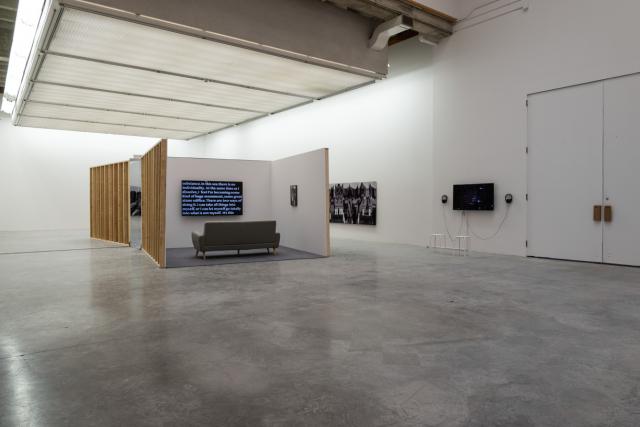 View of room with walls in middle and a TV with a couch, and art lined across wall