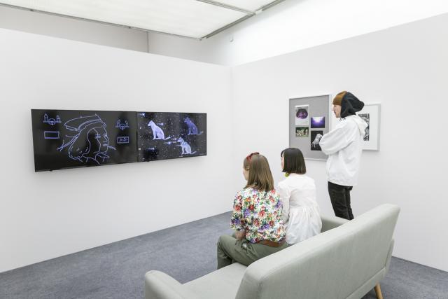 Two people sitting on a couch and one person standing up while watching a video installation from The Beyond Within