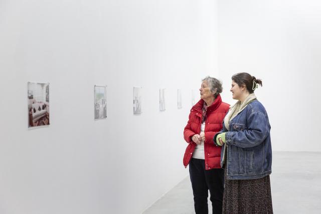 Two people standing up looking at photography on the wall hung up in a line