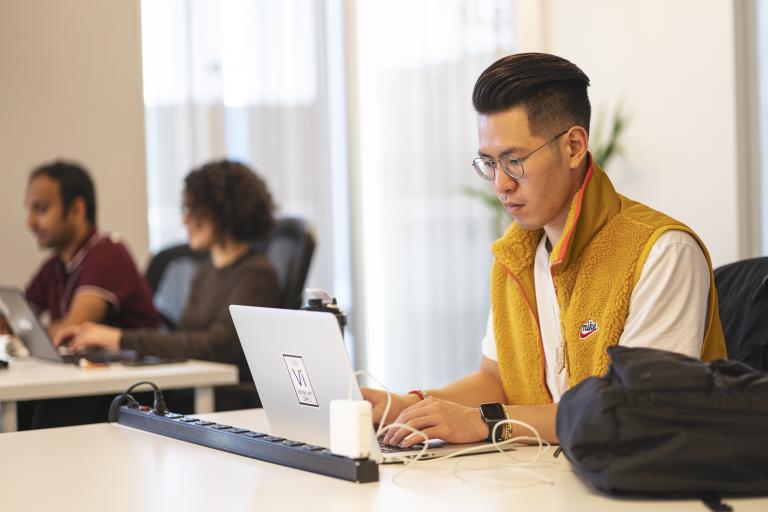 Man in a yellow vest working on a computer in an office