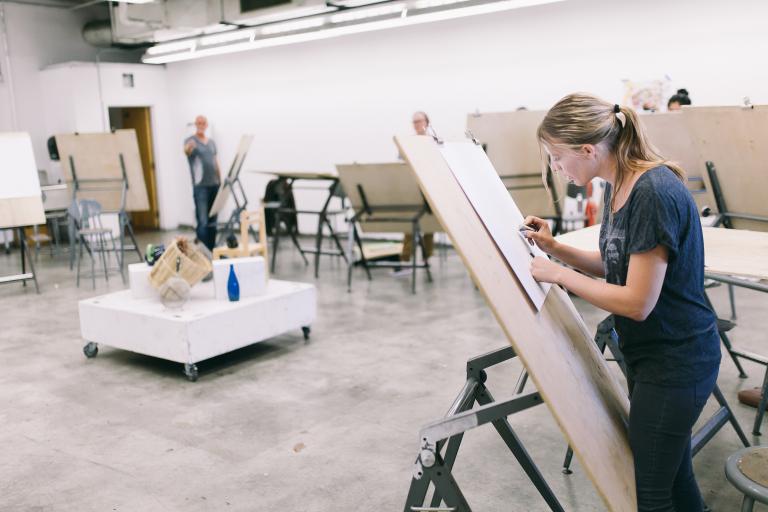 student drawing on a tilted drafting table in an art studio