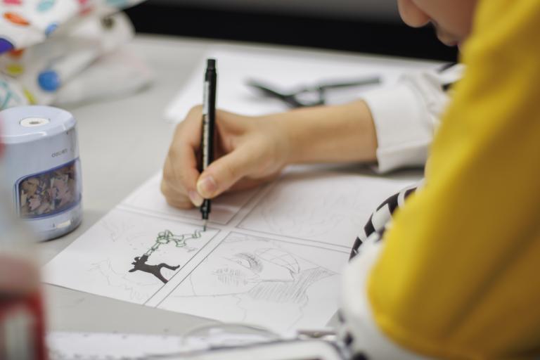 drawing student with a yellow t-shirt works on a series of gridded comic book drawings