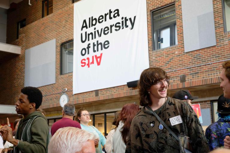 Students gather in AUArts’ main hall during orientation, chatting under a large Alberta University of the Arts banner.
