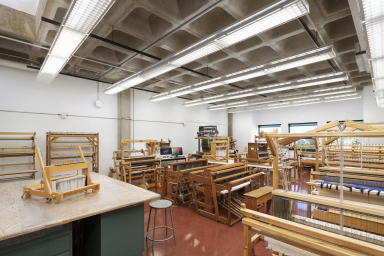 Fibre Studio AUArts fibre studio with rows of wooden floor looms and weaving equipment in a bright, spacious classroom.