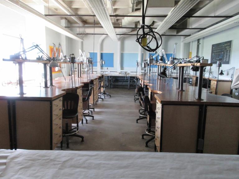Jewellery Studio 2 Jewellery studio with rows of wooden workbenches, task lamps, and chairs, set up for students to create and work on projects.