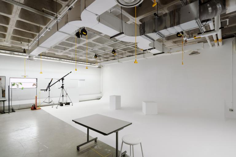 Photo Studio 1 A bright white photo studio with seamless white walls and floor, overhead lighting, and equipment including tripods, a crane arm, and stools.