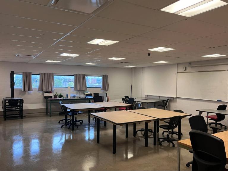 VCD Home Studio AUArts Visual Communication Design studio with large tables, rolling chairs, bright lighting, windows, and a whiteboard for collaborative work.